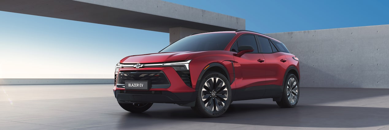 Vista frontal del Chevrolet Blazer RS EV 2025 en color rojo, estacionado frente a arquitectura moderna